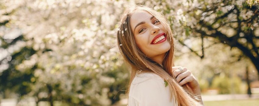 mulher bonita a sorrir num campo de primavera com as árvores em flor em pano de fundo